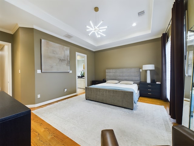 bedroom featuring ensuite bathroom, wood-type flooring, a chandelier, ornamental molding, and a tray ceiling