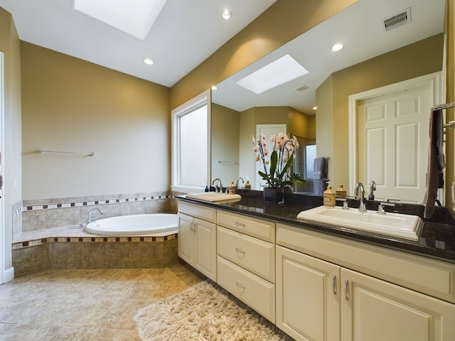 bathroom featuring tiled tub, vanity, tile patterned floors, and a skylight