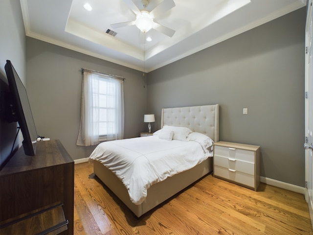 bedroom with ceiling fan, ornamental molding, light hardwood / wood-style floors, and a tray ceiling