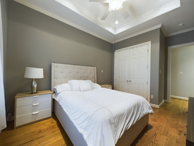 bedroom featuring ceiling fan, a tray ceiling, crown molding, light wood-type flooring, and a closet