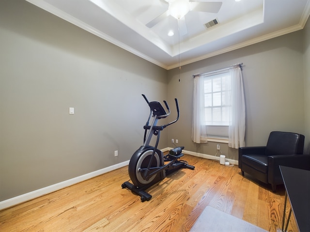 workout room with crown molding, light hardwood / wood-style flooring, and a raised ceiling