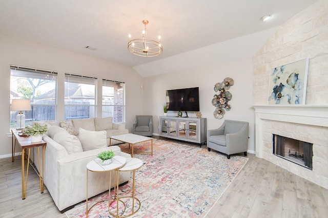 living room with hardwood / wood-style flooring, a stone fireplace, a chandelier, and vaulted ceiling