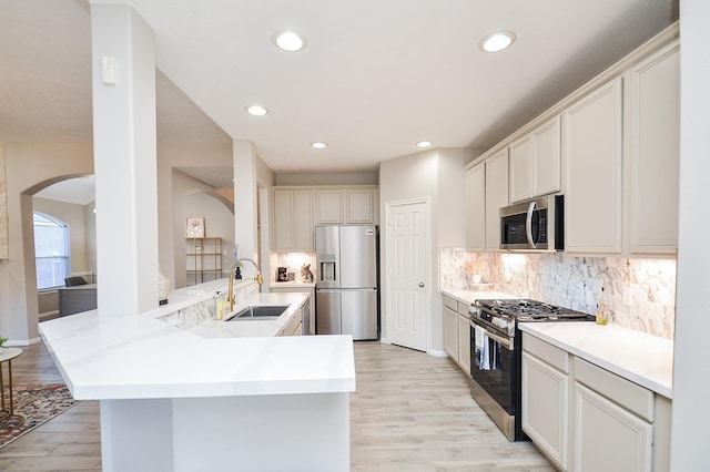 kitchen featuring sink, appliances with stainless steel finishes, kitchen peninsula, light hardwood / wood-style floors, and decorative backsplash