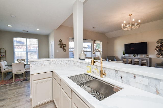 kitchen with lofted ceiling, light hardwood / wood-style flooring, white cabinetry, a notable chandelier, and decorative light fixtures