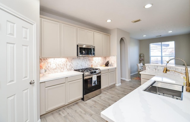 kitchen with tasteful backsplash, sink, light wood-type flooring, and appliances with stainless steel finishes