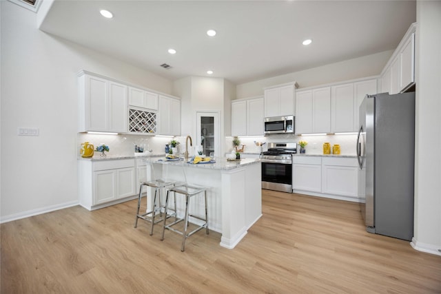 kitchen with appliances with stainless steel finishes, white cabinets, a kitchen island with sink, and a breakfast bar