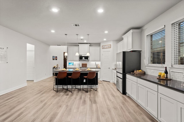 kitchen featuring pendant lighting, appliances with stainless steel finishes, white cabinetry, a center island, and a kitchen bar