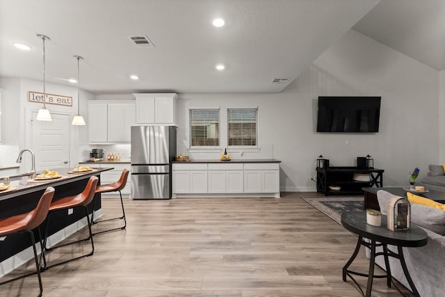 kitchen with hanging light fixtures, stainless steel refrigerator, white cabinets, and light wood-type flooring