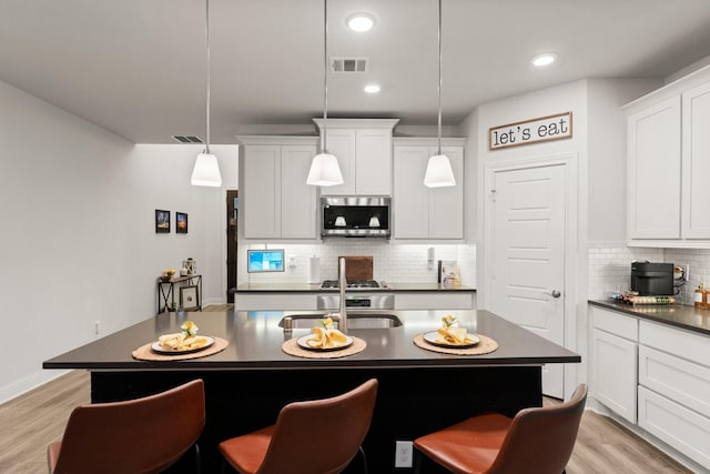 kitchen featuring a kitchen bar, tasteful backsplash, an island with sink, pendant lighting, and light hardwood / wood-style floors