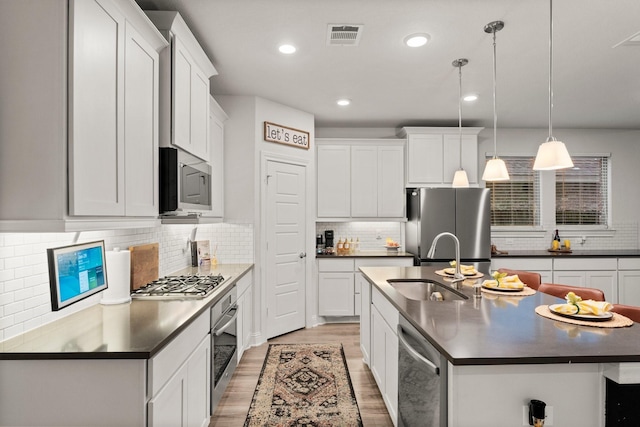 kitchen featuring white cabinetry, appliances with stainless steel finishes, hanging light fixtures, and a center island with sink