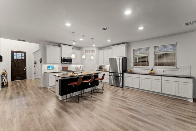 kitchen with white cabinets, a kitchen breakfast bar, hanging light fixtures, stainless steel appliances, and a center island with sink