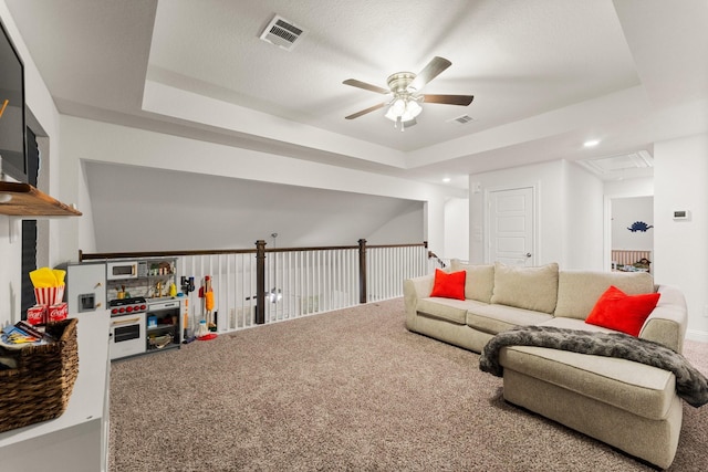 living room with a tray ceiling, ceiling fan, and carpet flooring