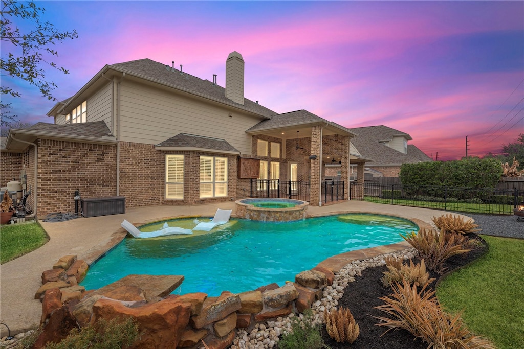 pool at dusk with an in ground hot tub and a patio area