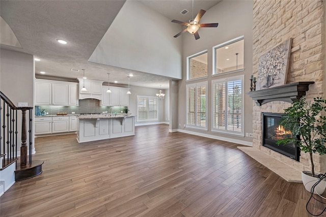 living area with light wood finished floors, baseboards, stairway, a fireplace, and ceiling fan with notable chandelier