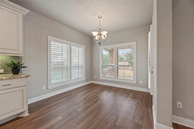 unfurnished dining area featuring a chandelier, dark wood finished floors, a textured ceiling, and baseboards