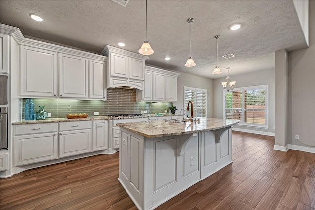 kitchen featuring light stone countertops, a center island with sink, white cabinets, and decorative light fixtures