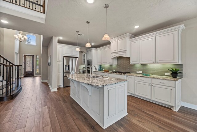 kitchen featuring a center island with sink, white cabinets, light stone counters, appliances with stainless steel finishes, and a sink