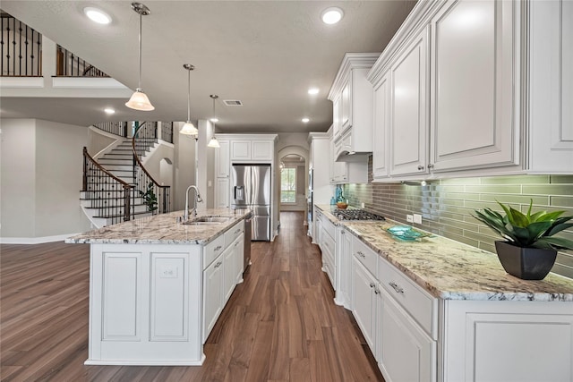 kitchen with white cabinets, appliances with stainless steel finishes, decorative light fixtures, a kitchen island with sink, and a sink