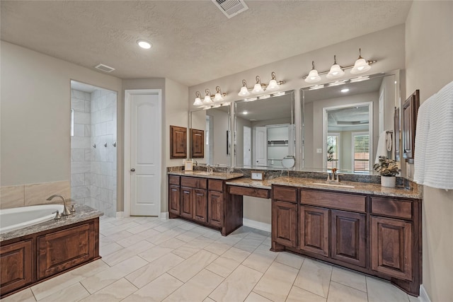 bathroom with a garden tub, visible vents, two vanities, and a sink