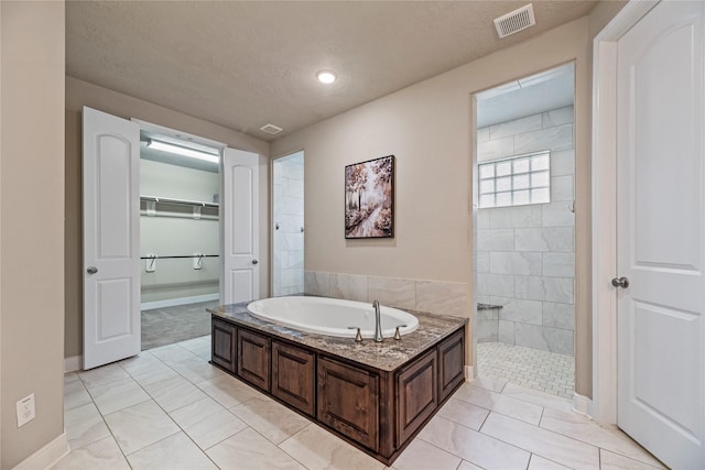 bathroom with a walk in closet, a garden tub, visible vents, a textured ceiling, and tiled shower