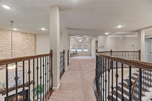 hallway with a textured ceiling, an upstairs landing, baseboards, carpet, and attic access