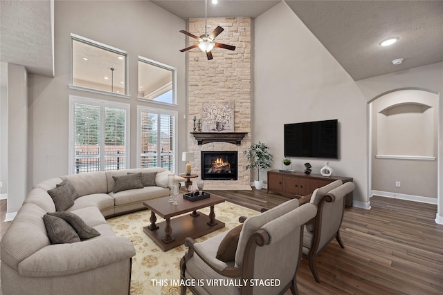 living area featuring baseboards, ceiling fan, wood finished floors, a fireplace, and high vaulted ceiling