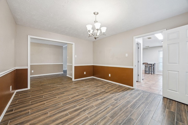 spare room with dark wood-type flooring, an inviting chandelier, and a textured ceiling