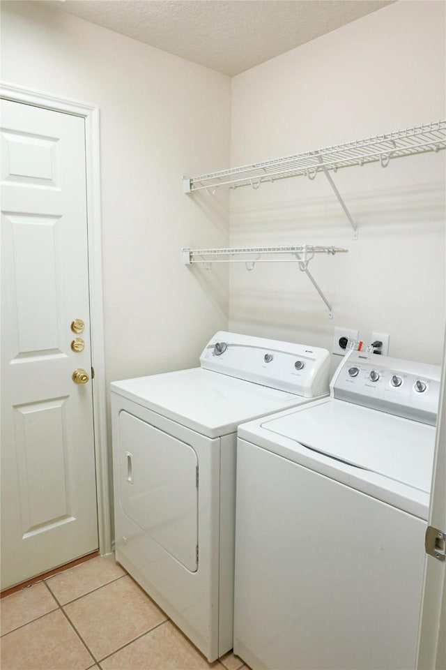 washroom with light tile patterned flooring, independent washer and dryer, and a textured ceiling