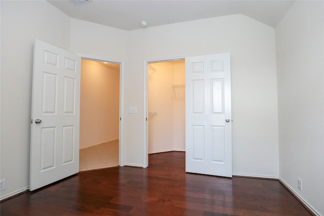 unfurnished bedroom with vaulted ceiling, a walk in closet, dark wood-type flooring, and a closet