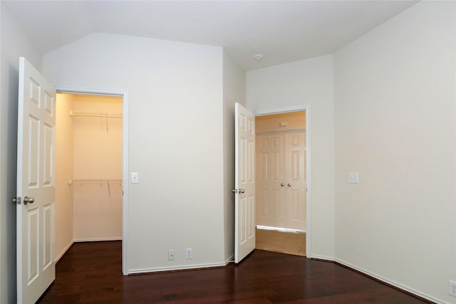 unfurnished bedroom with dark wood-type flooring, a walk in closet, a closet, and vaulted ceiling