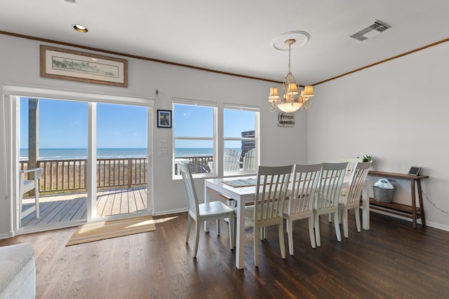 dining room with a view of the beach, dark wood-type flooring, ornamental molding, and a water view