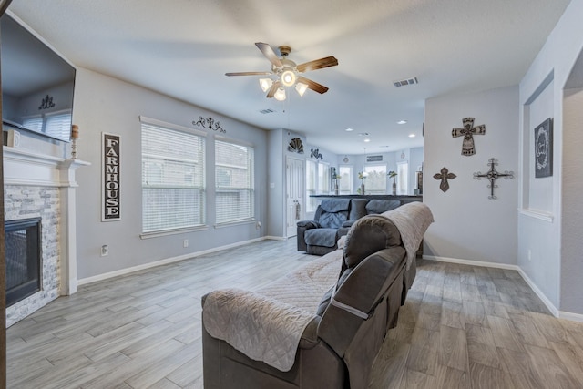 living room with ceiling fan, a stone fireplace, light hardwood / wood-style floors, and a healthy amount of sunlight