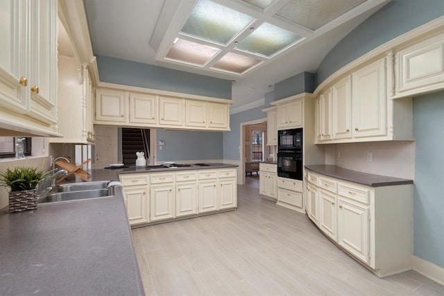 kitchen featuring sink, tasteful backsplash, black appliances, cream cabinetry, and light wood-type flooring