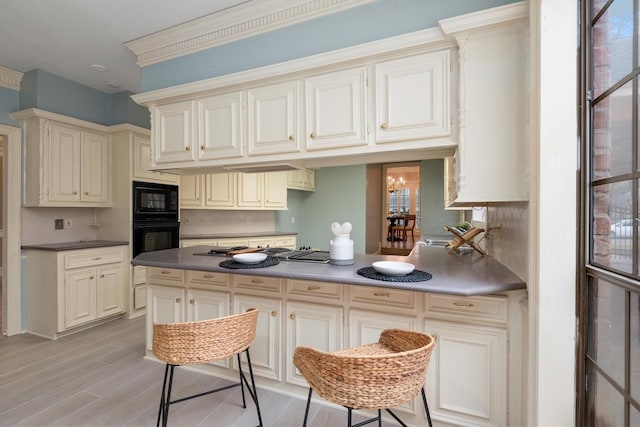 kitchen featuring backsplash, light hardwood / wood-style flooring, black appliances, and cream cabinetry