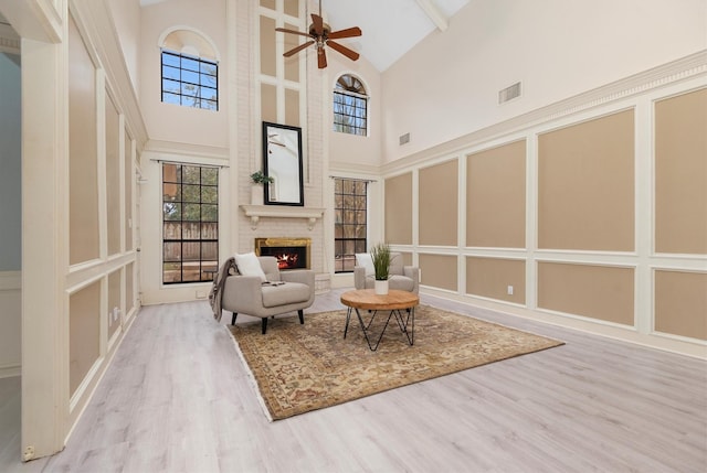 living area featuring high vaulted ceiling, a fireplace, light hardwood / wood-style floors, and ceiling fan