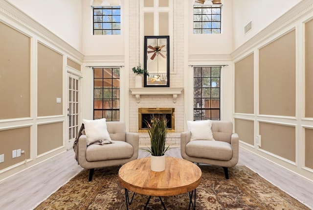 sitting room with a brick fireplace, a towering ceiling, plenty of natural light, and hardwood / wood-style floors