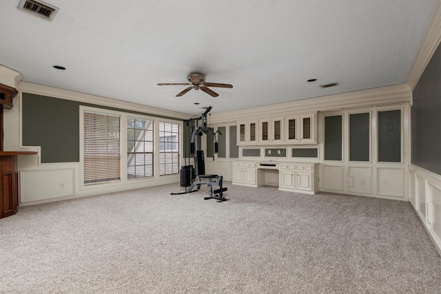 unfurnished room featuring ceiling fan, light colored carpet, ornamental molding, and built in desk