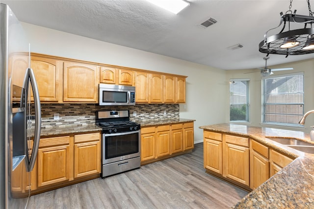 kitchen featuring sink, stainless steel appliances, light stone counters, light hardwood / wood-style floors, and decorative backsplash