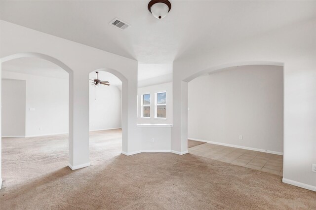 spare room featuring arched walkways, carpet floors, visible vents, baseboards, and a ceiling fan