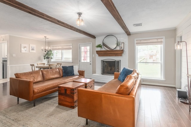 living room featuring a brick fireplace, an inviting chandelier, beam ceiling, and light hardwood / wood-style floors