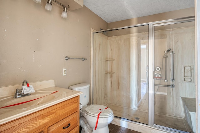 bathroom featuring vanity, a shower with shower door, toilet, and a textured ceiling