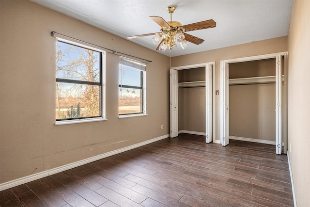 unfurnished bedroom with two closets, dark hardwood / wood-style floors, and ceiling fan