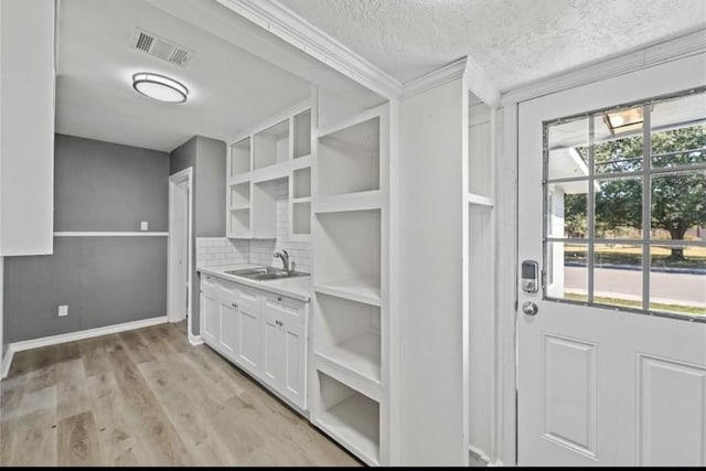 kitchen featuring tasteful backsplash, sink, light wood-type flooring, white cabinets, and a textured ceiling