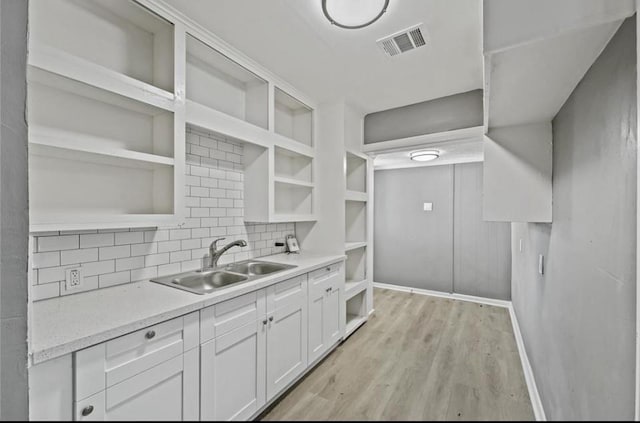 kitchen featuring tasteful backsplash, white cabinetry, sink, light stone countertops, and light wood-type flooring