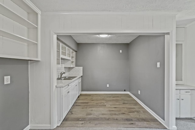 kitchen with sink, white cabinets, a textured ceiling, and light hardwood / wood-style flooring