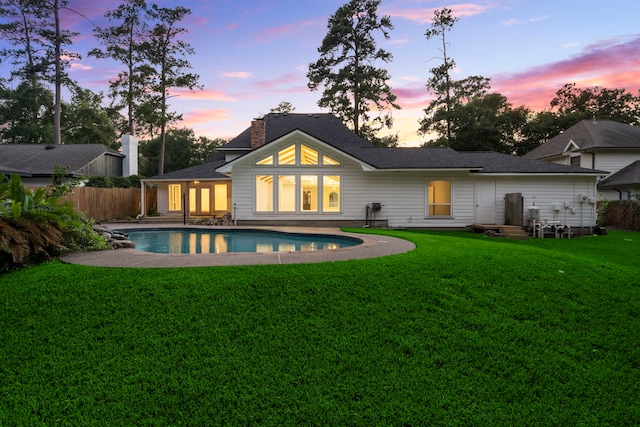 back house at dusk with a patio and a lawn