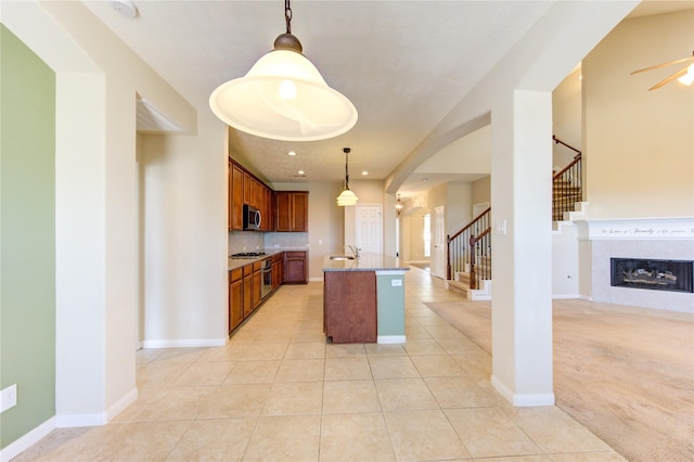 kitchen with pendant lighting, light tile patterned floors, appliances with stainless steel finishes, a center island with sink, and a tiled fireplace