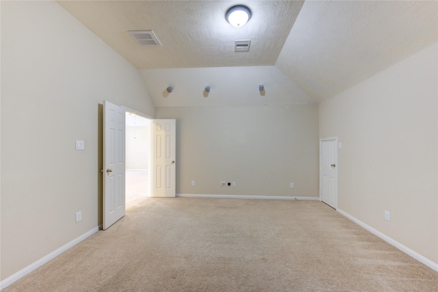 empty room featuring lofted ceiling, light carpet, and a textured ceiling