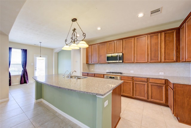 kitchen featuring sink, an island with sink, pendant lighting, stainless steel appliances, and light stone countertops