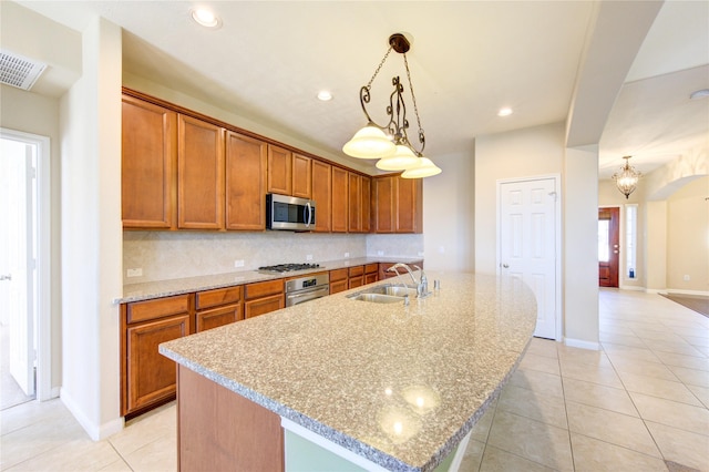 kitchen featuring sink, backsplash, stainless steel appliances, a center island with sink, and decorative light fixtures